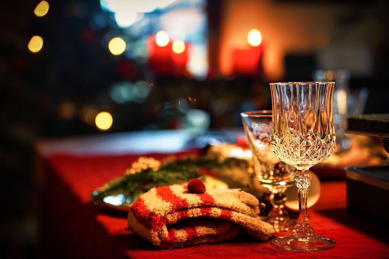 A festive table with crystal glasses, red candles, and striped mittens, adorned with Christmas decorations. - Home Instead