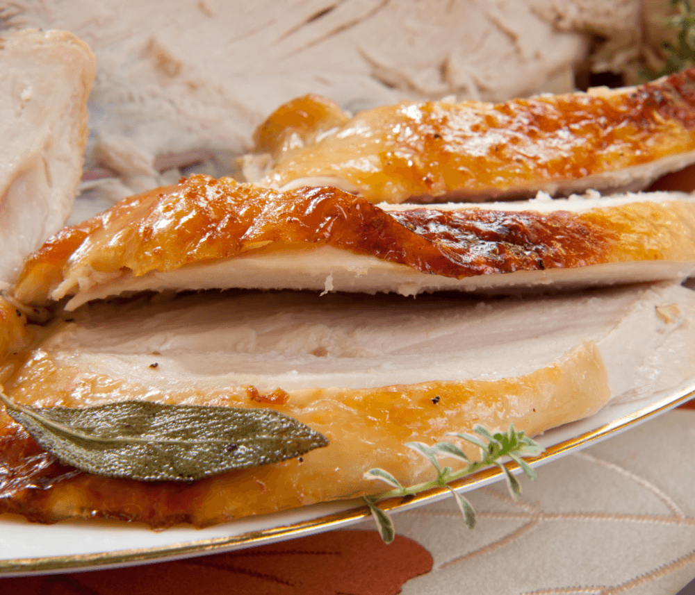 Sliced roasted turkey breast with golden-brown skin, garnished with herbs, served on a white plate. - Home Instead