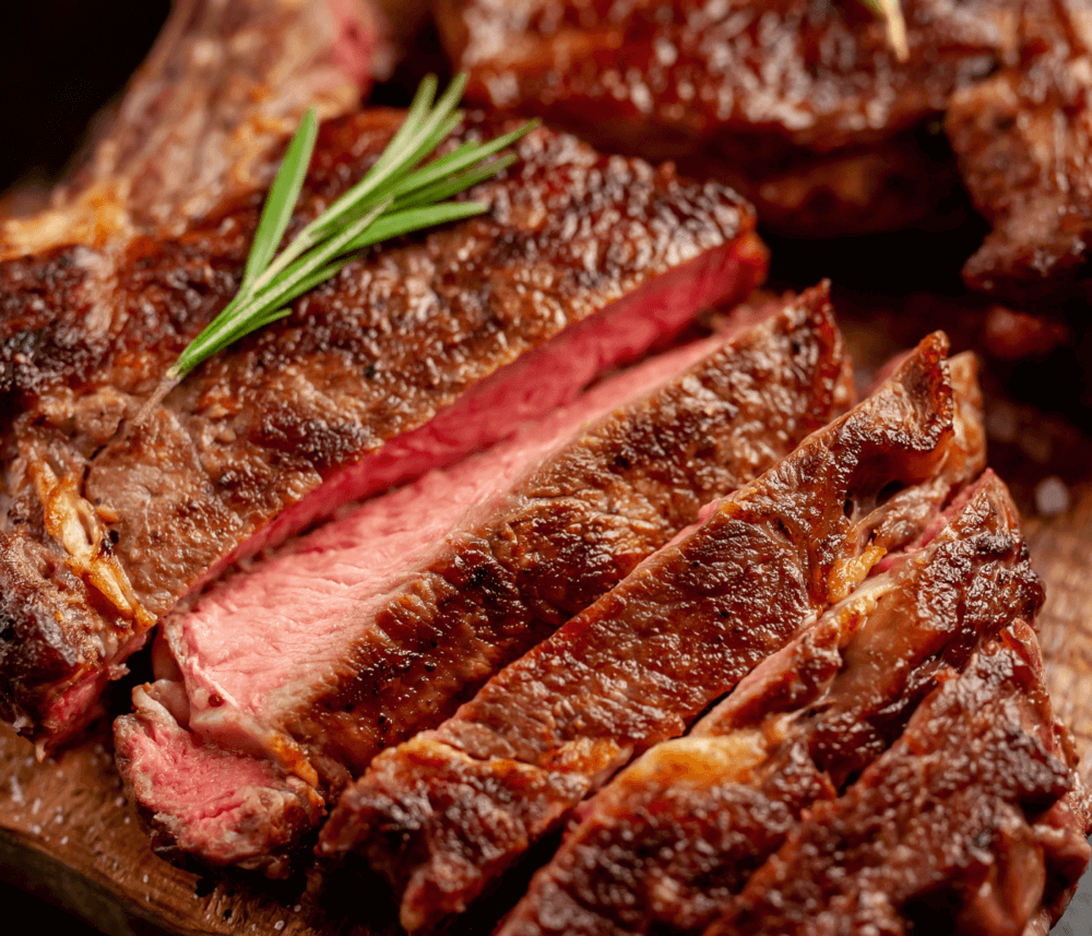 Sliced medium-rare steak garnished with rosemary on a wooden board. - Home Instead