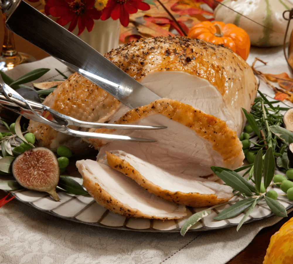 A knife carving a roasted turkey breast on a festive plate with figs, greenery, and pumpkins in the background. - Home Instead