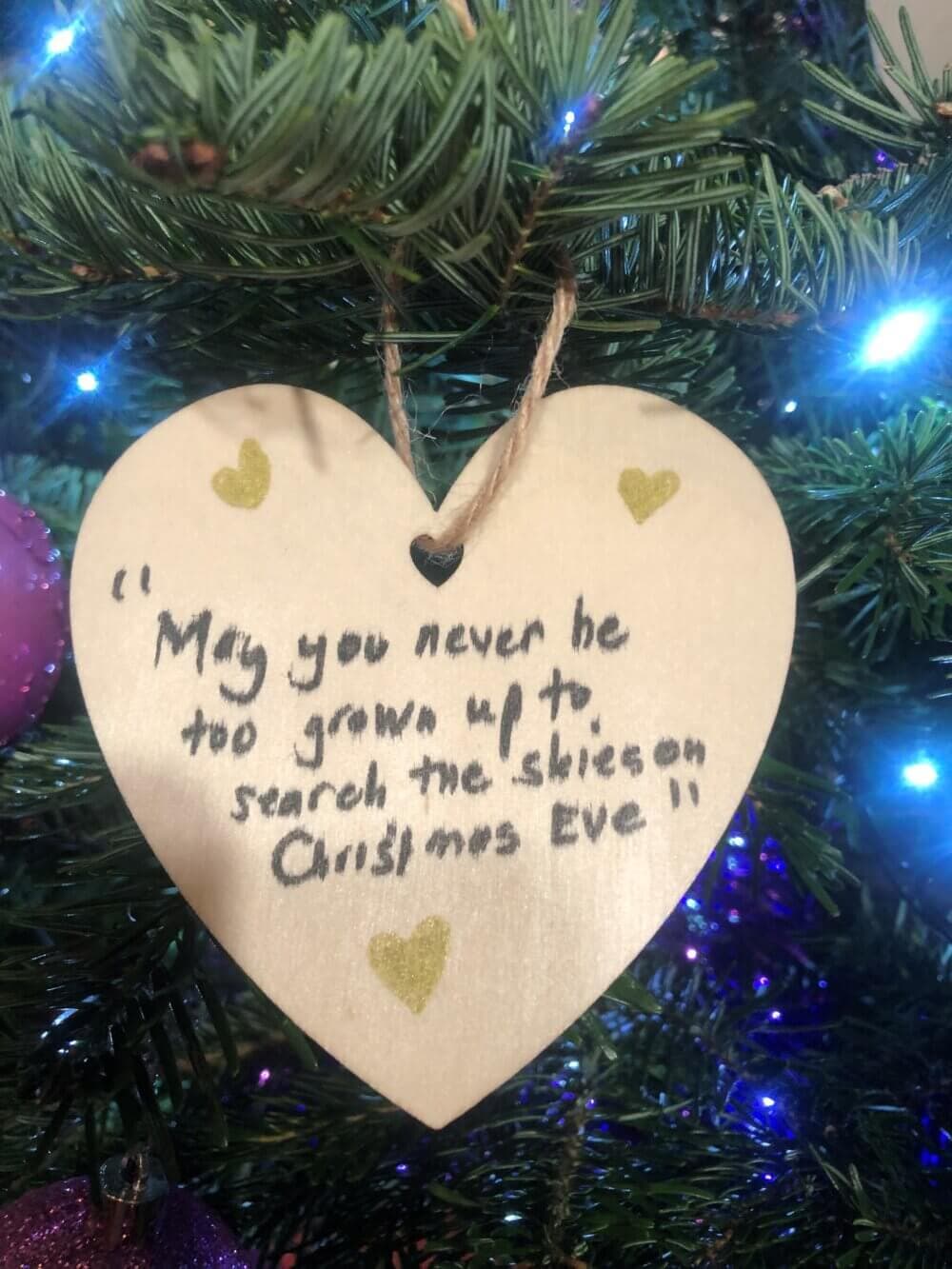 Heart-shaped ornament on a Christmas tree with the quote: "May you never be too grown up to search the skies on Christmas Eve. - Home Instead