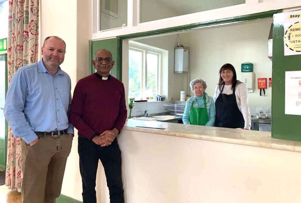 Four people standing in a community kitchen, two men on the left and two women on the right behind the counter. - Home Instead