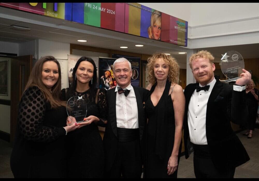Five people in formal attire smiling and holding awards at an indoor event. - Home Instead