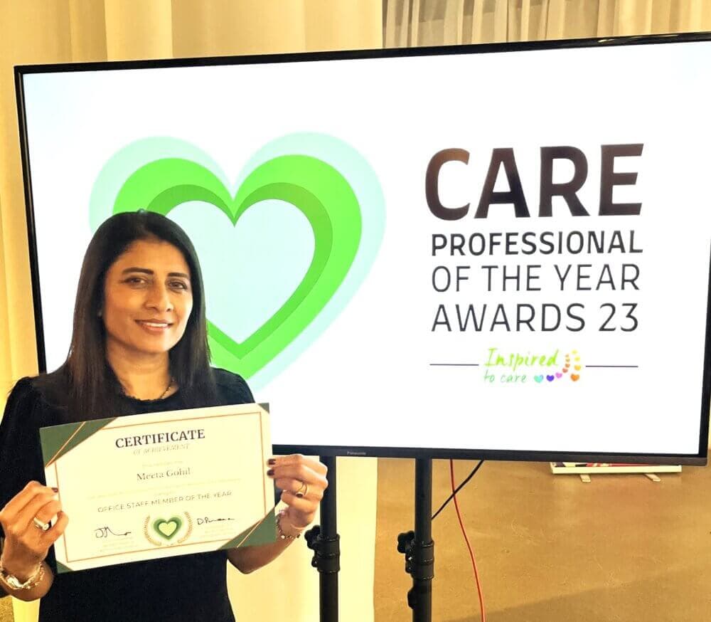 A woman holds a certificate in front of a screen displaying "Care Professional of the Year Awards 23. - Home Instead