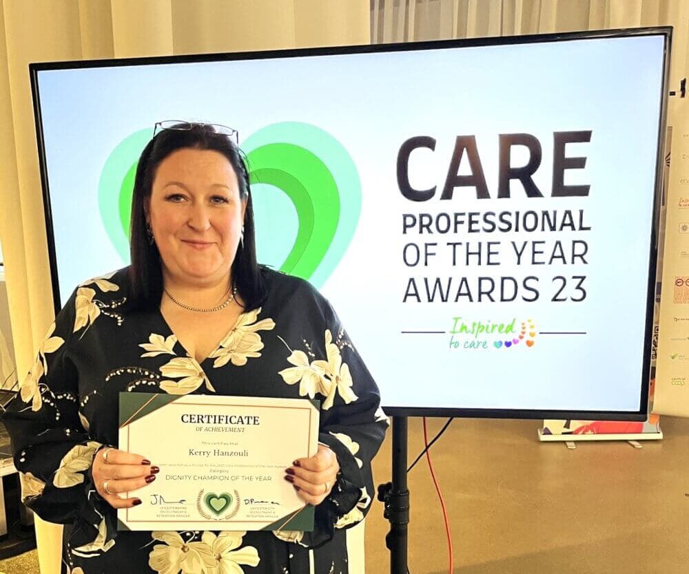 A woman holding a certificate, standing in front of a screen that reads "CARE Professional of the Year Awards 23". - Home Instead