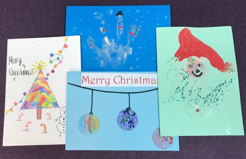 Four colorful handmade Christmas cards featuring drawings of a tree, ornaments, snowmen, and a festive face. - Home Instead