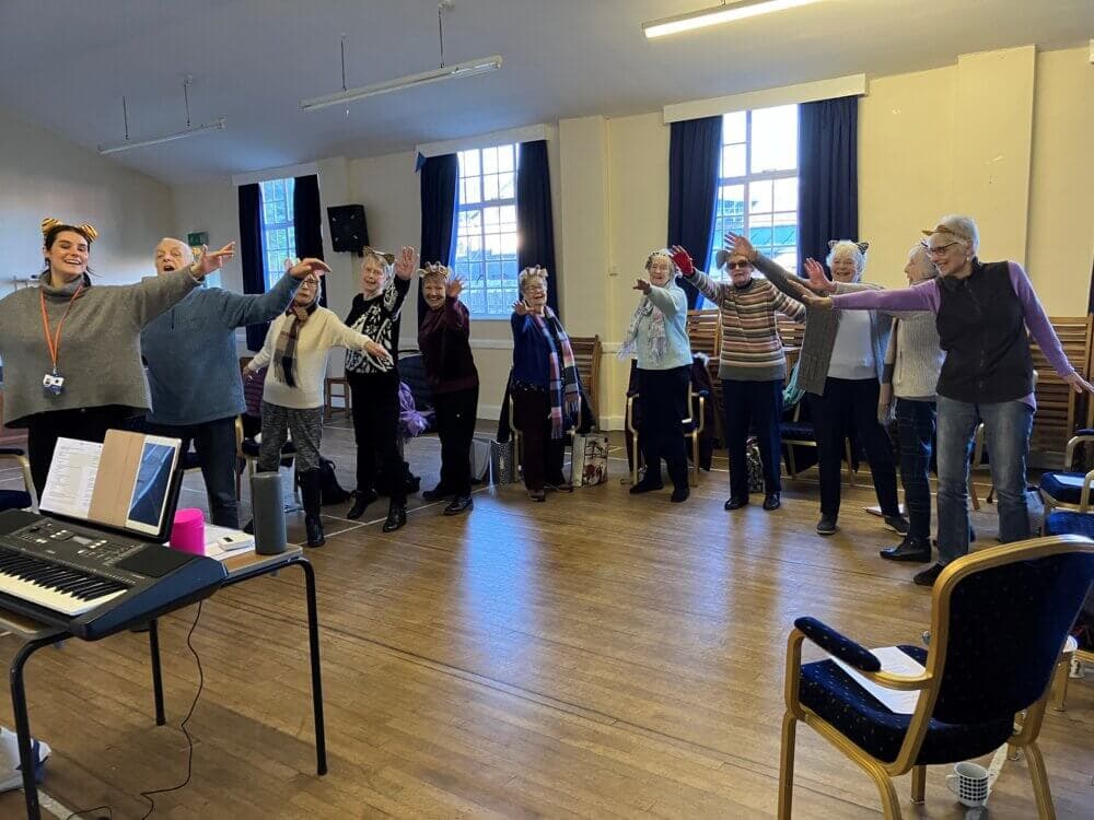 A group of people standing in a semi-circle in a room, raising their right hands in unison, with a keyboard in the foreground. - Home Instead