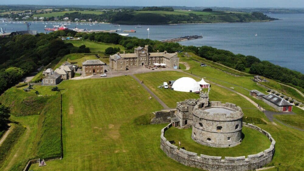 Aerial view of a historic castle on green hills by the ocean, with surrounding buildings and scenic coastal landscape. - Home Instead