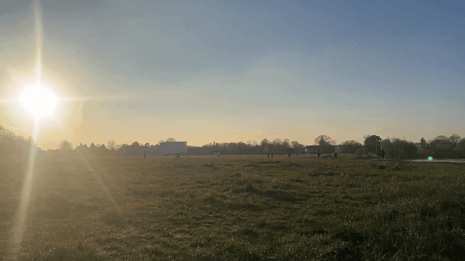 The image shows a sunrise over a grassy field with a few people scattered in the distance. The sky is clear. - Home Instead