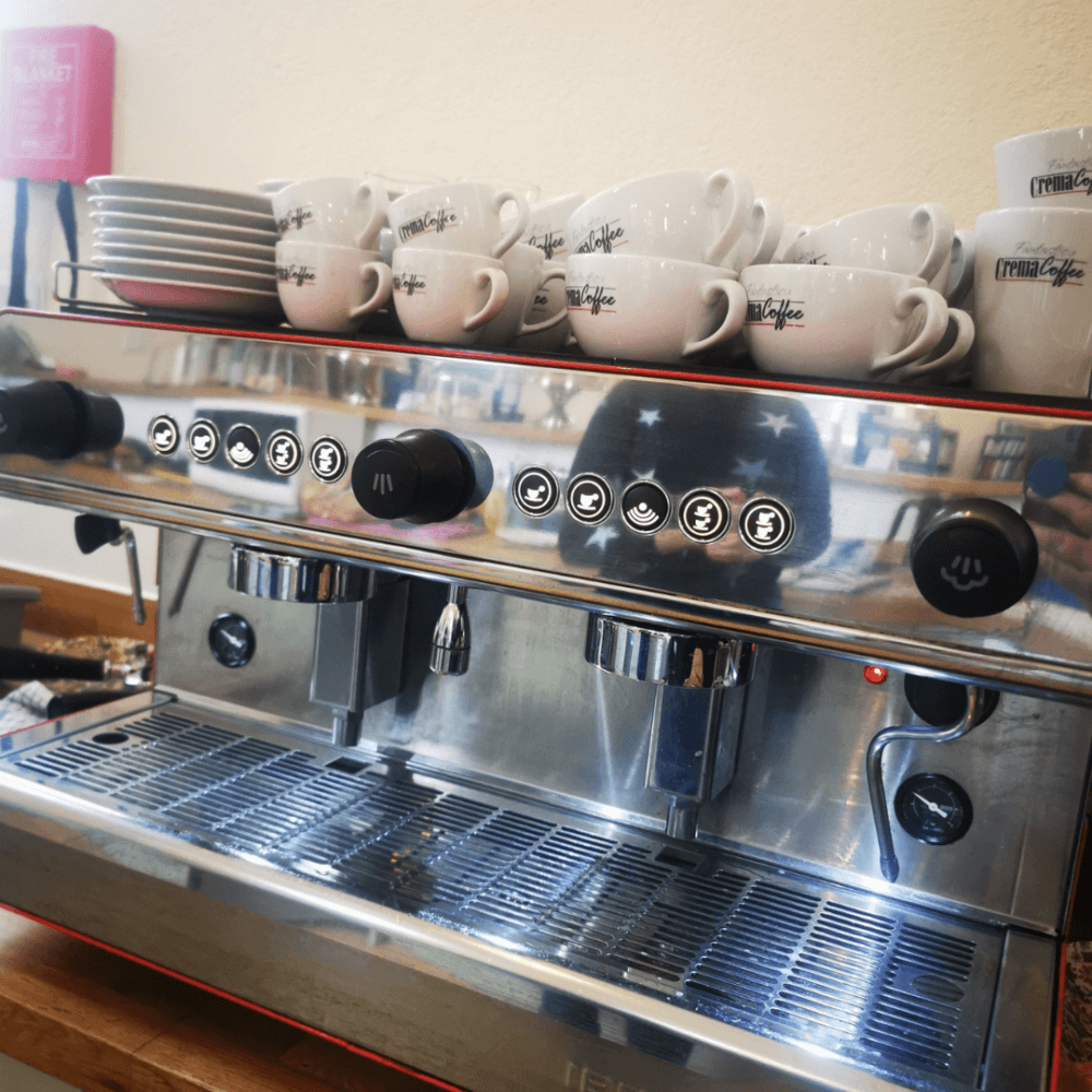 Stainless steel espresso machine with coffee cups on top and various control buttons on the front panel. - Home Instead