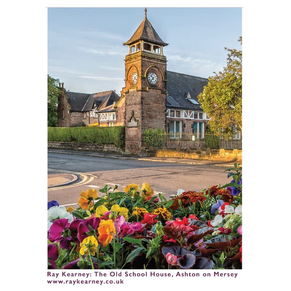 The Old School House with a clock tower, surrounded by colorful flowers in Ashton on Mersey. - Home Instead