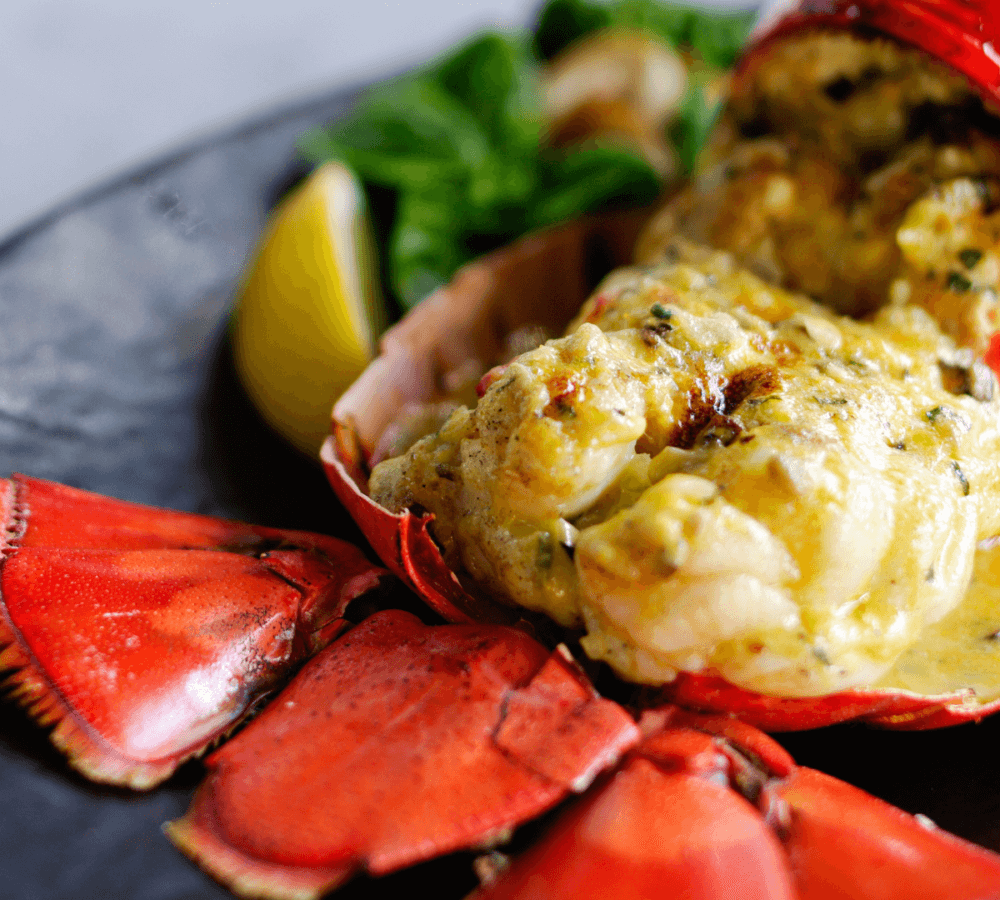 A close-up of a gourmet dish of stuffed lobster tail, garnished with lemon wedges and greens. - Home Instead
