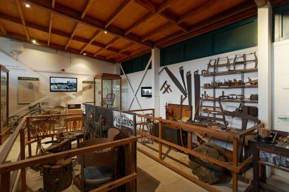 Interior of a wooden-roofed museum exhibit displaying various antique tools, farming equipment, and historical artifacts. - Home Instead