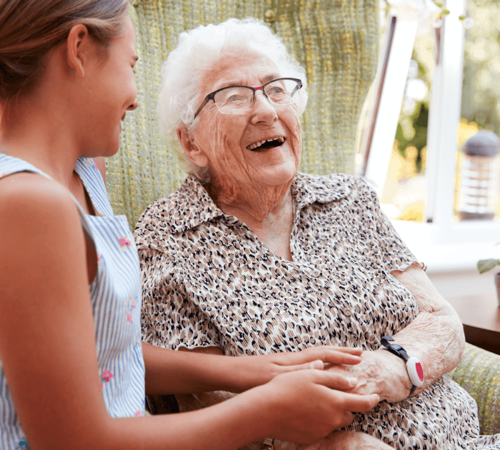 Elderly woman laughing and holding hands with a young girl in a bright, cozy room. - Home Instead