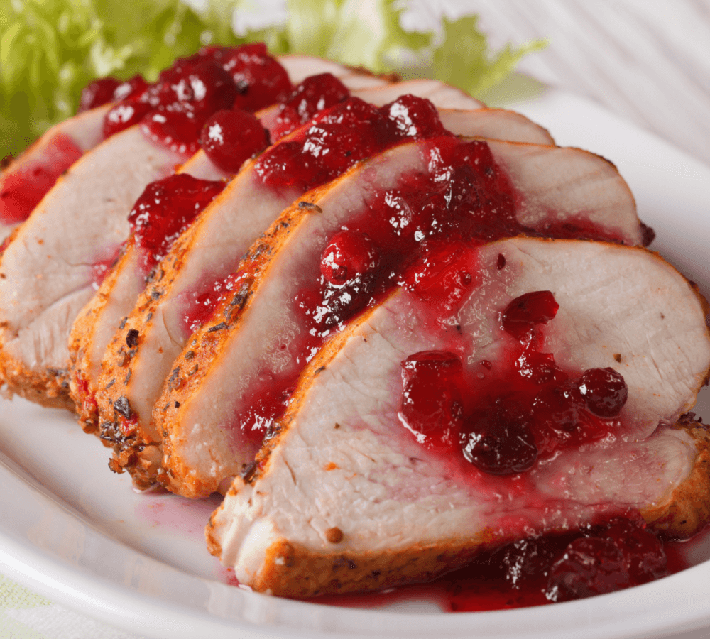 Sliced roast turkey topped with cranberry sauce, served on a white plate with a garnish of lettuce in the background. - Home Instead