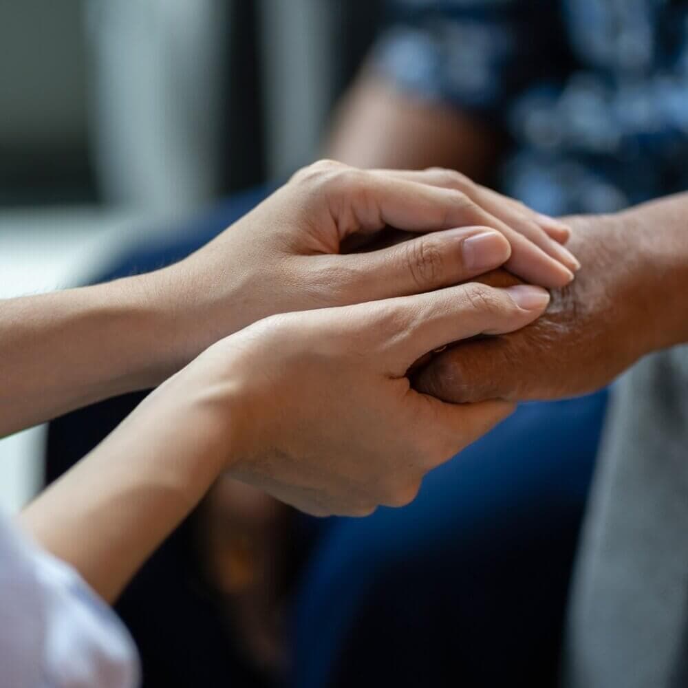 A close-up of two pairs of hands clasping each other, showing a gesture of support and care. - Home Instead