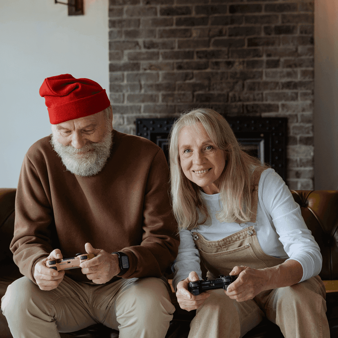 Elderly couple playing video games together sat beside each other on a sofa