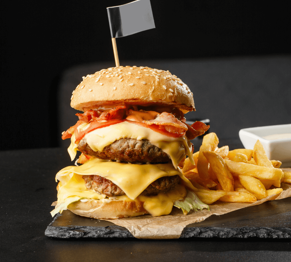 A double cheeseburger with bacon, lettuce, and tomato, served with fries on a slate plate. - Home Instead