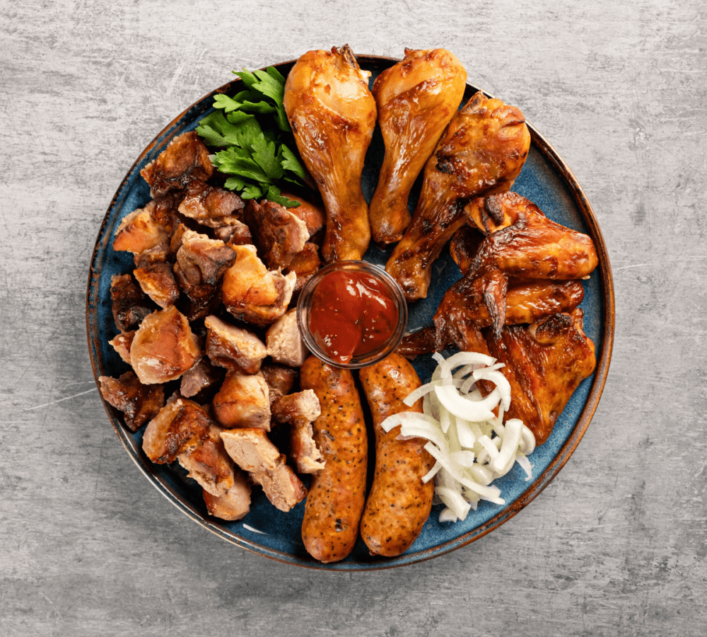 A plate of assorted grilled meats including chicken drumsticks, wings, sausages, chopped meat, garnished with parsley and onions. - Home Instead