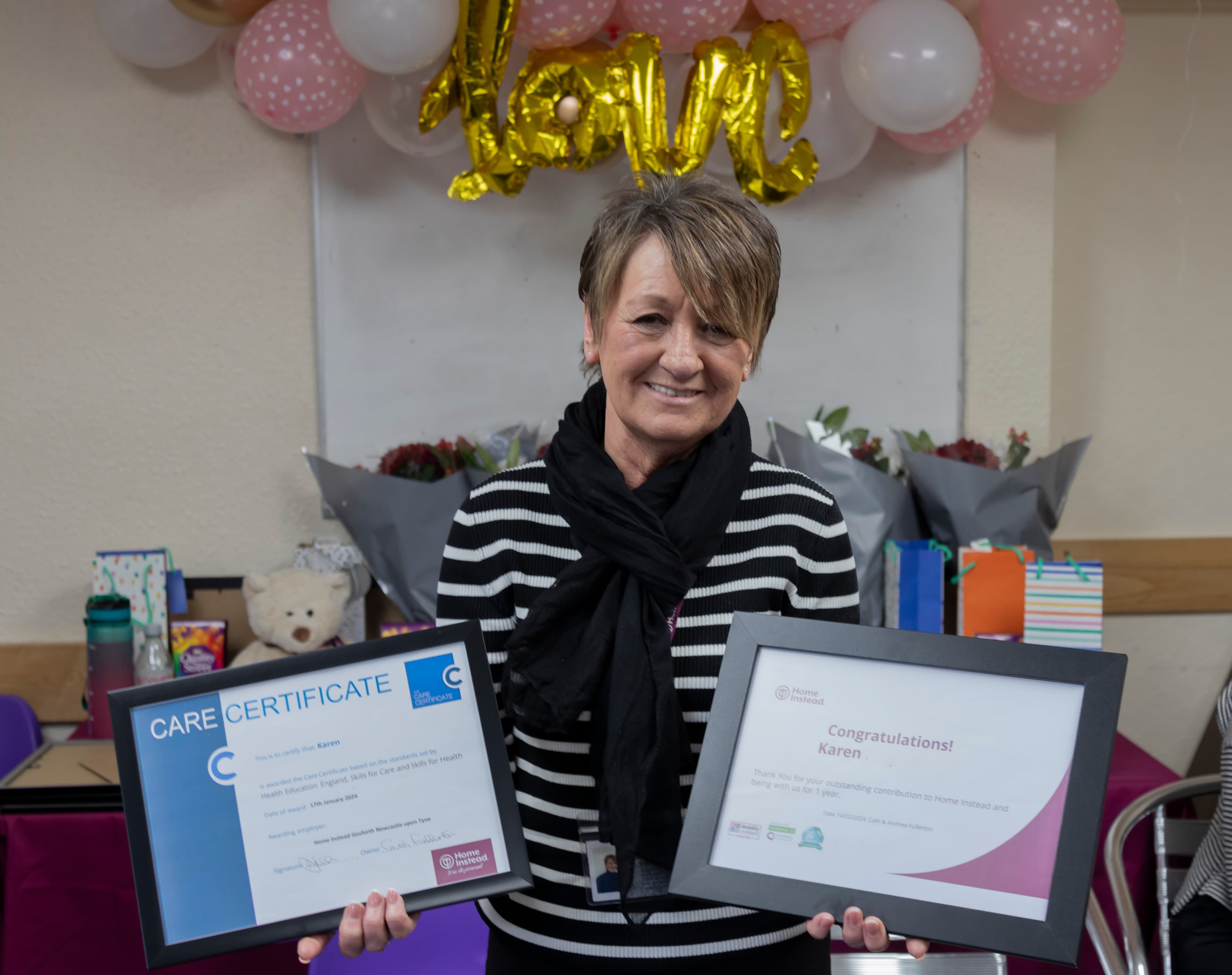 A person smiling and holding certificates, with festive decorations and gift bags in the background. - Home Instead