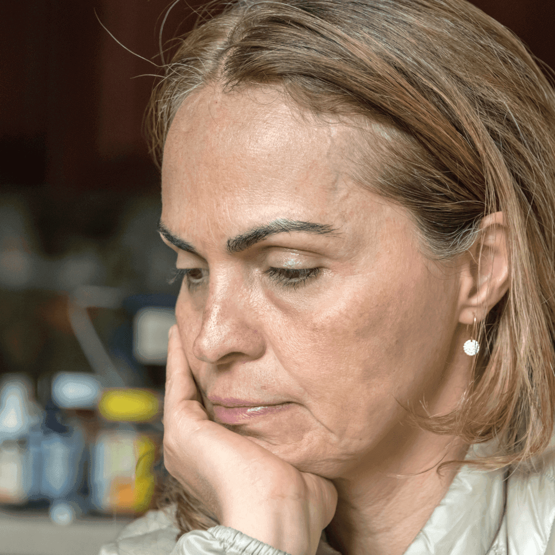 A person with long hair and earrings rests their chin on their hand, appearing reflective or pensive. - Home Instead