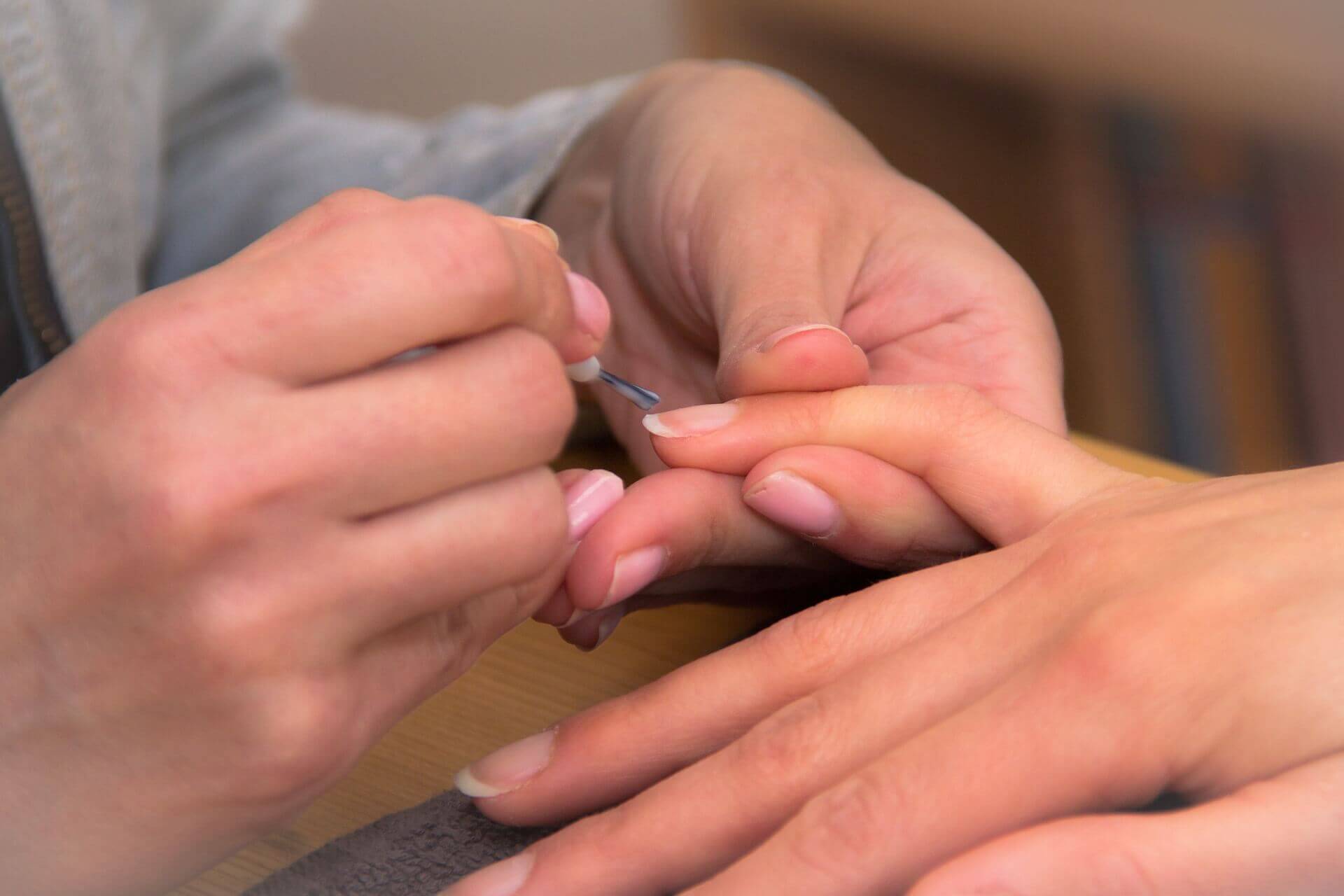 Close-up of a person applying clear nail polish to another person's fingernails. - Home Instead