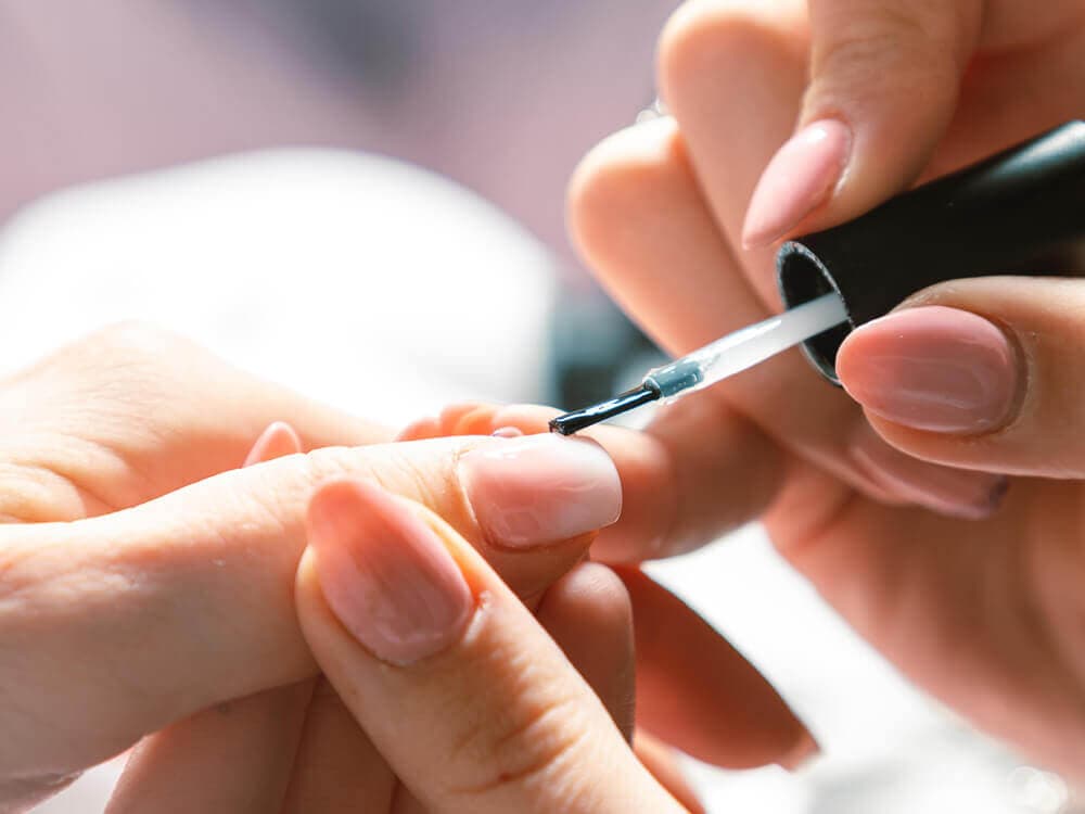 Close-up of a manicure in progress, with a person applying clear nail polish to someone's fingernail. - Home Instead