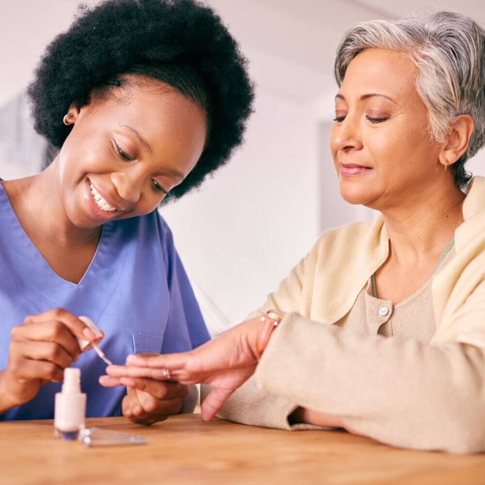 A care professional helping an older woman with her nail care.