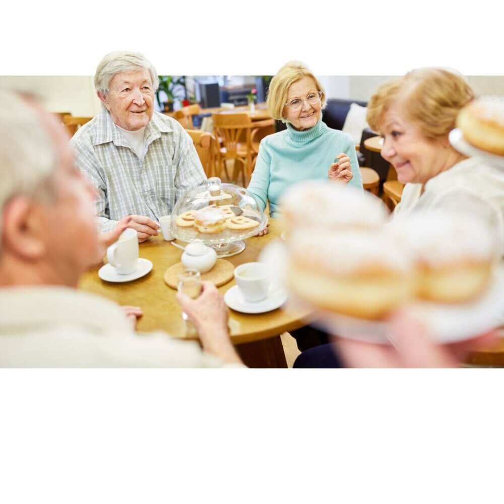 Four seniors enjoying tea and pastries together at a cozy cafe. - Home Instead