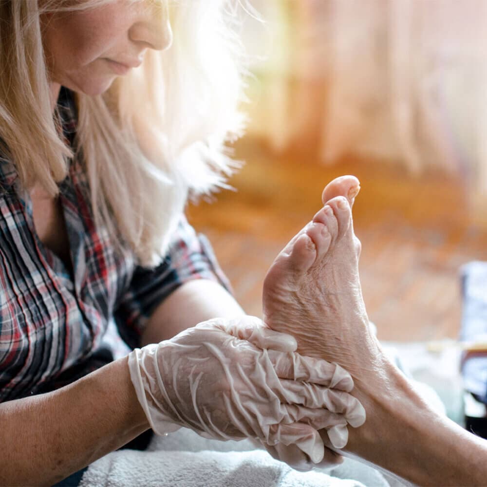 A care professional giving a foot massage to an elderly client in the comfort of her home.