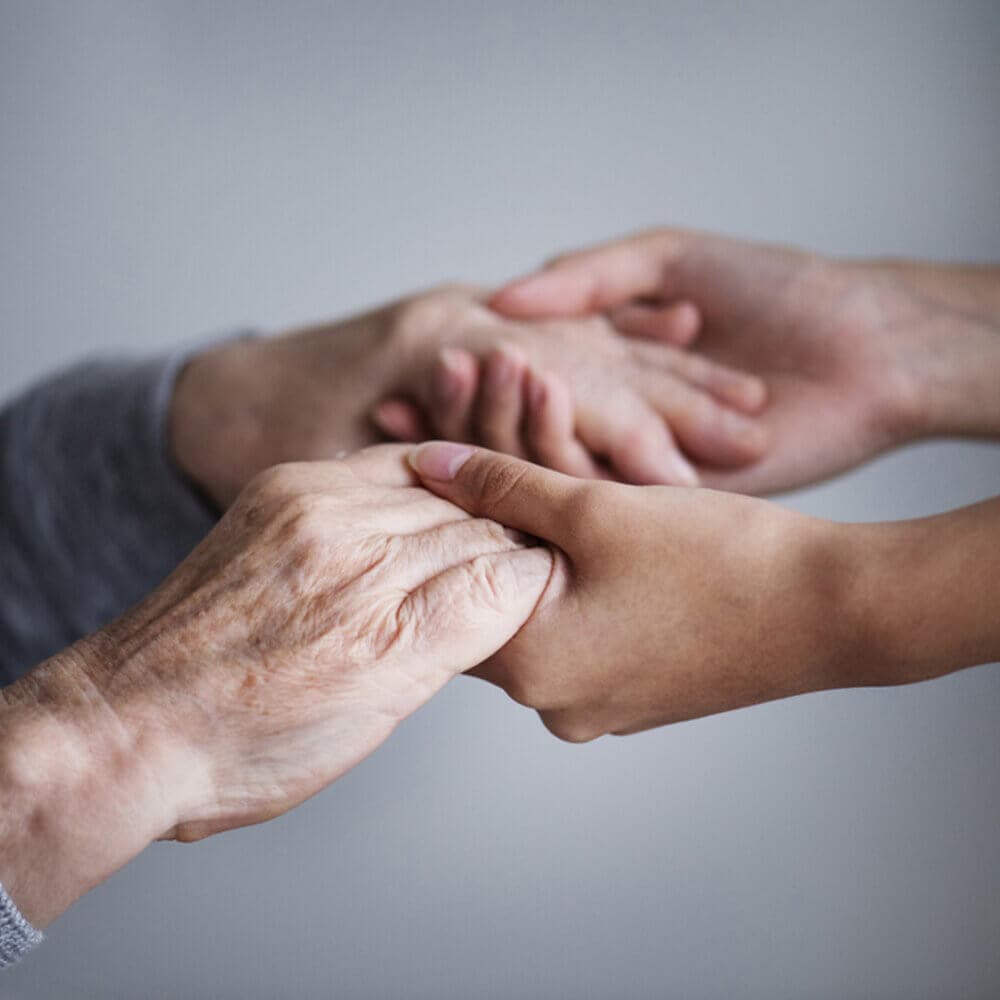 Two people, young and old, holding each other's hands in support of one another.
