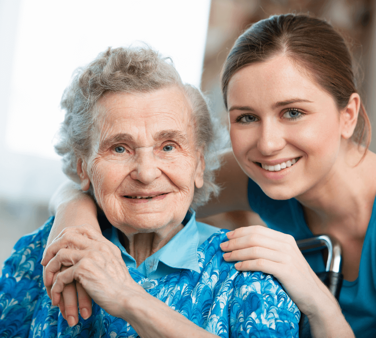 Elderly woman smiling with a younger woman who has her arm around the elderly woman in a comforting manner. - Home Instead