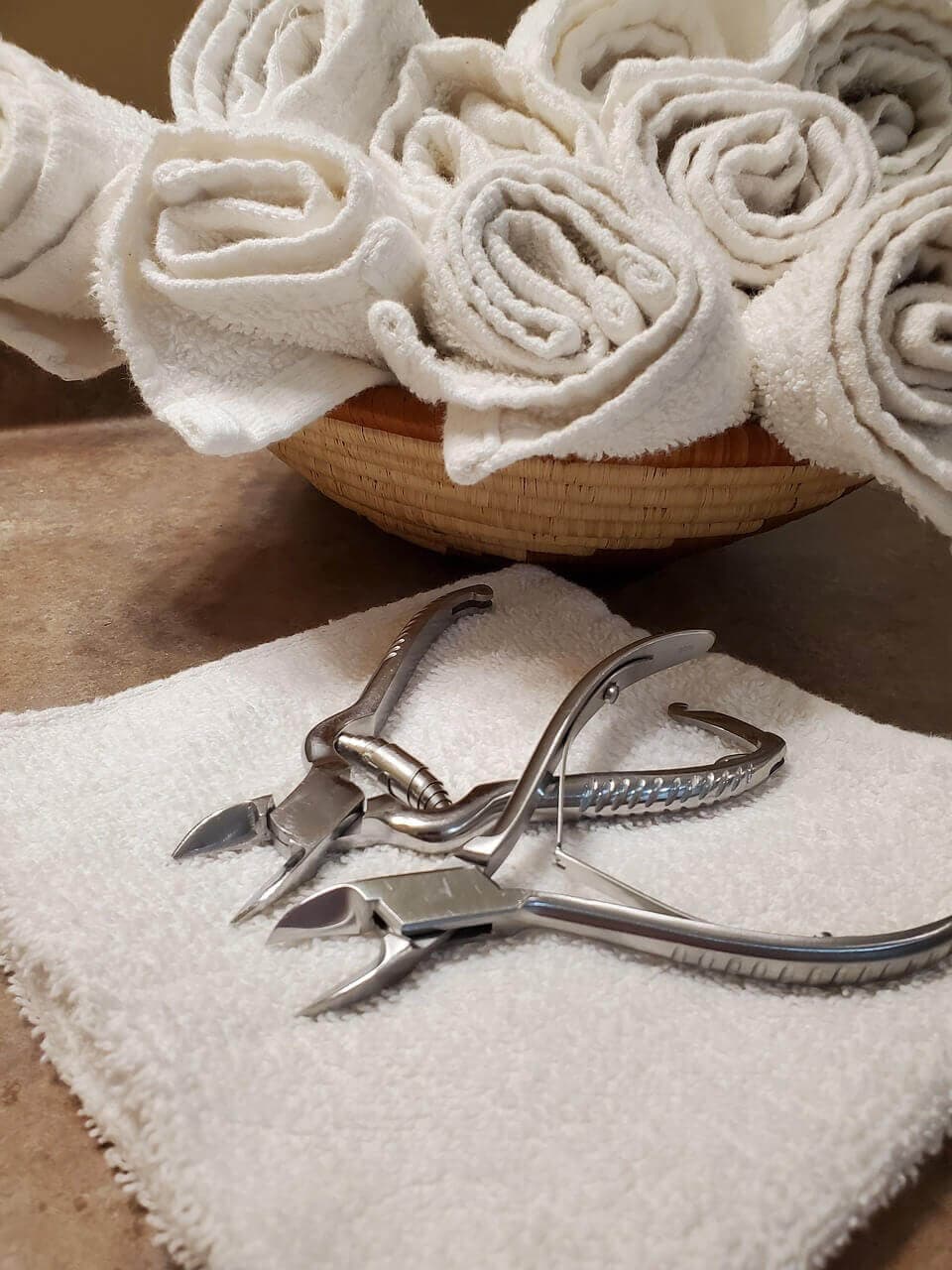 Rolled white towels in a basket with manicure tools placed on a towel in the foreground. - Home Instead