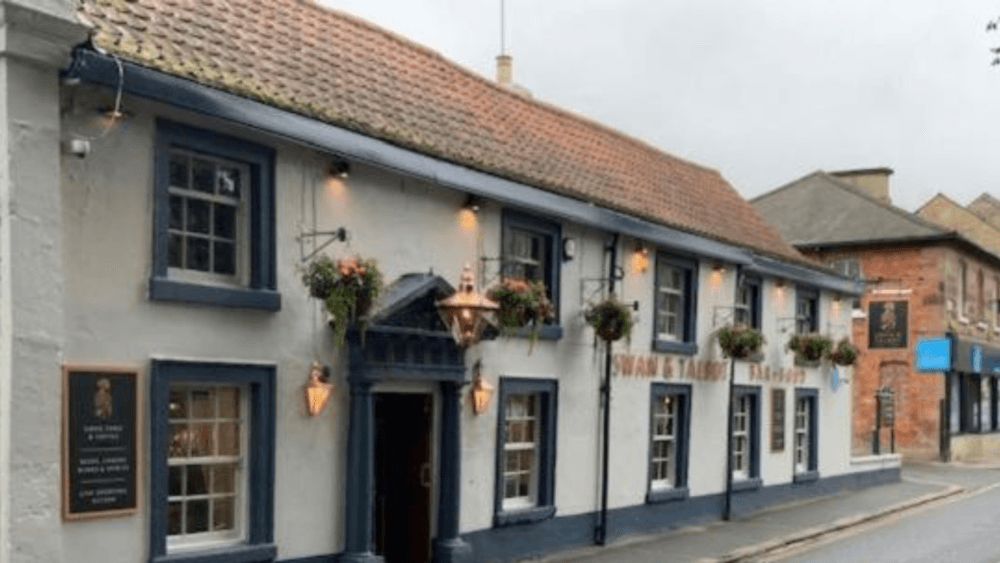 A quaint, old-fashioned pub with hanging flower baskets and a tiled roof on a quiet street. - Home Instead