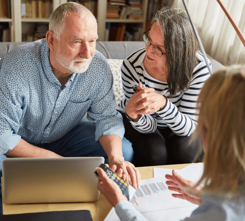An older couple examines financial documents on a table with a financial advisor, holding a calculator. - Home Instead