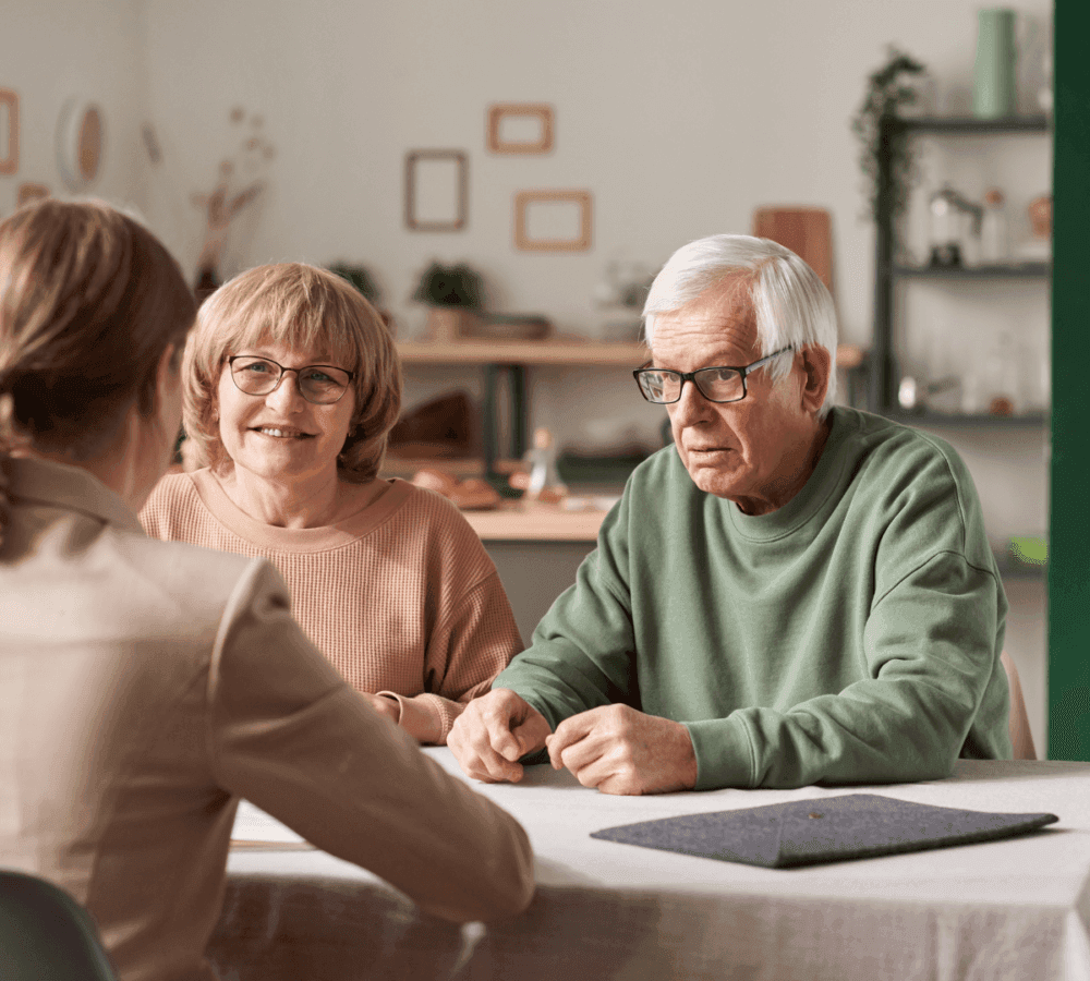Three people sitting at a table in a meeting. The two on the far side are older adults, the person on the near side is younger. - Home Instead