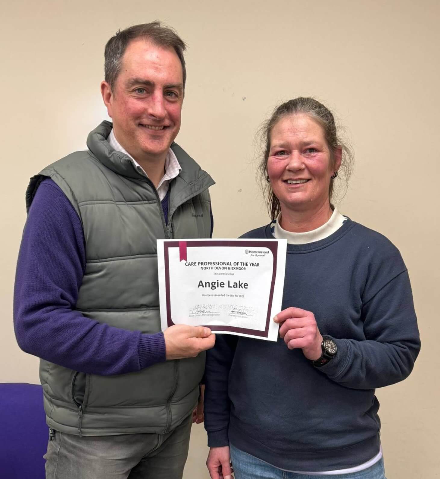 Two people smiling; one is holding a "Care Professional of the Year" certificate awarded to Angie Lake. - Home Instead