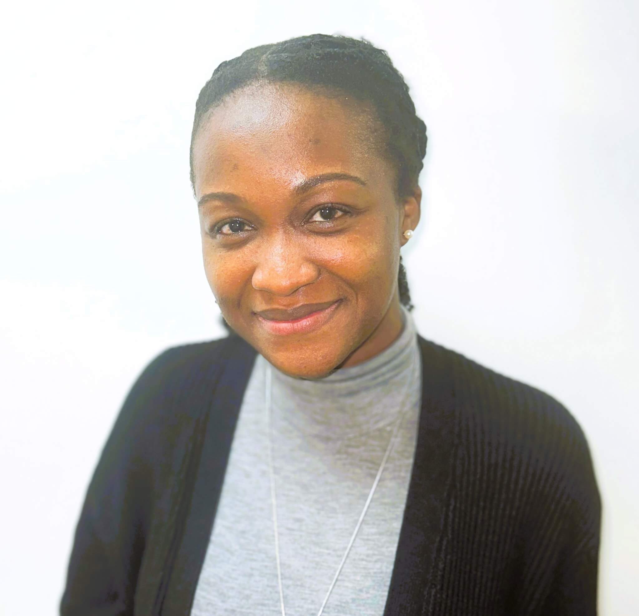 Smiling person with neatly braided hair wearing a gray turtleneck and black cardigan against a plain white background. - Home Instead