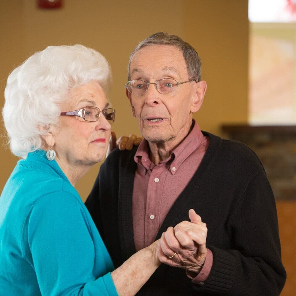 An elderly couple dances together, holding hands and looking content. - Home Instead