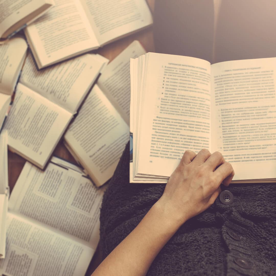 Person reading a book with scattered open books on the floor, viewed from above. - Home Instead