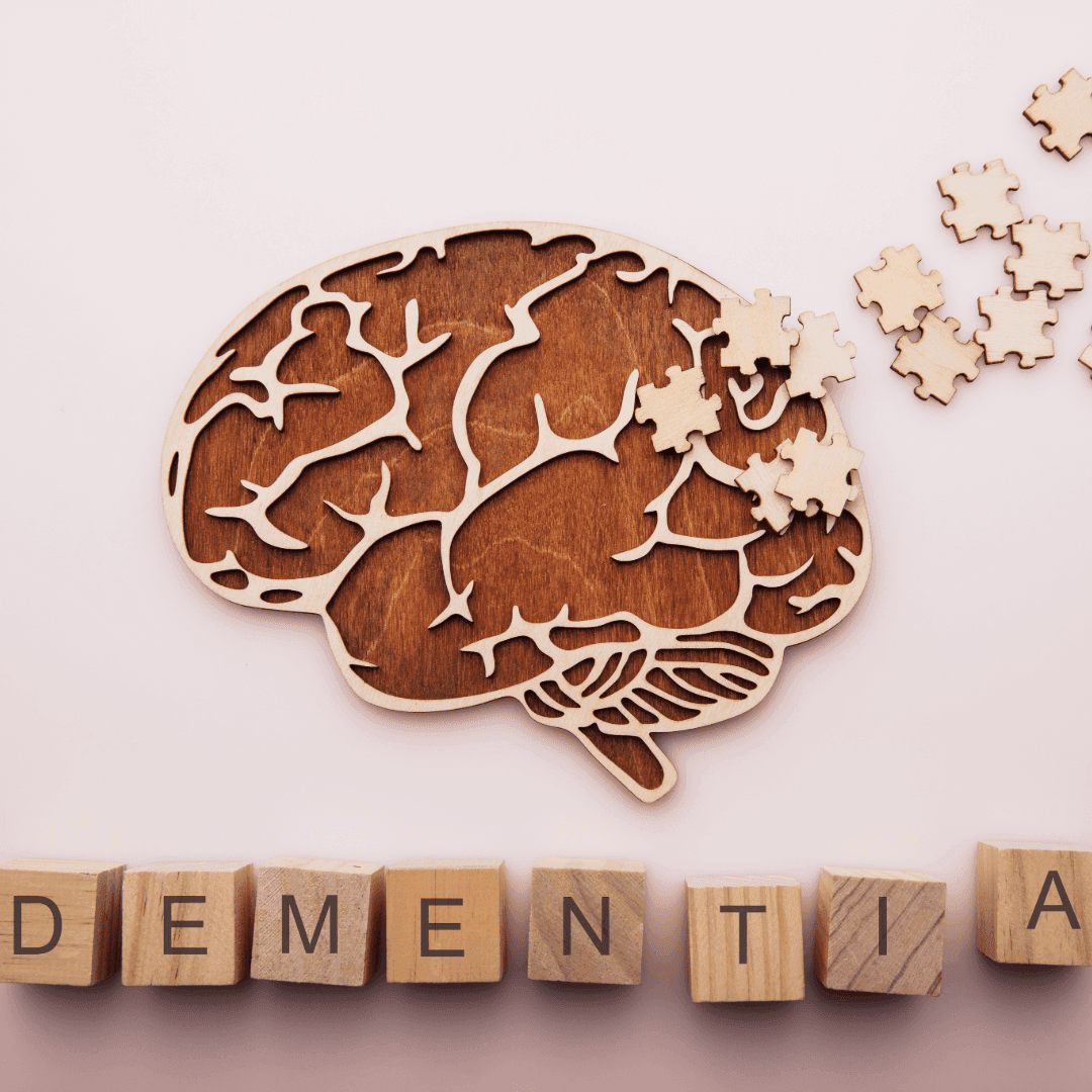 Wooden brain puzzle with pieces missing, next to wooden blocks spelling "DEMENTIA" on a light background. - Home Instead