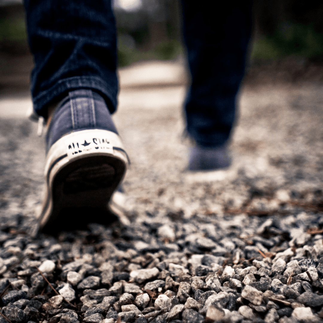 Close-up of a person walking on a gravel path, focusing on their sneakers and lower legs. - Home Instead