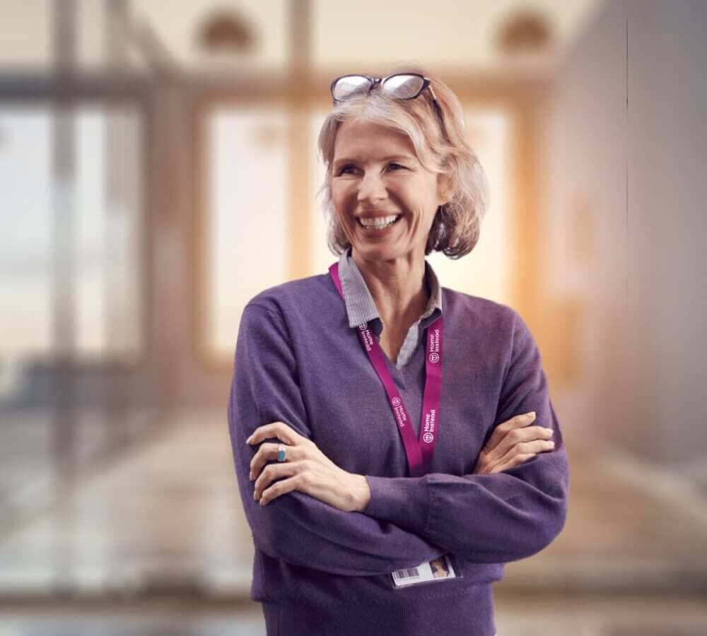 A female Home Instead Care Professional stands smiling and looking off to the left.