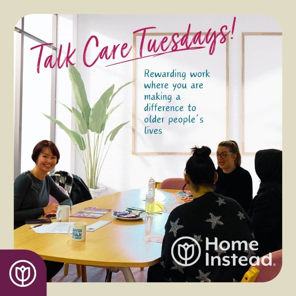 Group discussion at a table with a sign reading "Talk Care Tuesdays!" about rewarding work with older people, with Home Instead logo. - Home Instead