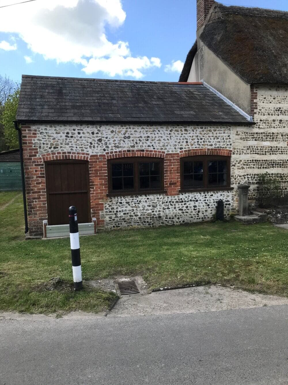 A small, old stone building with a brown door, three windows, and a black-and-white striped post in front of it. - Home Instead
