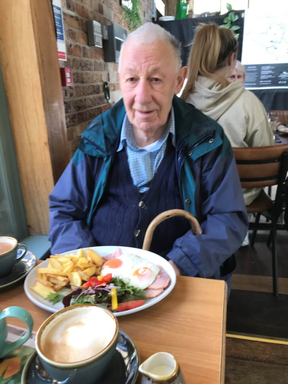 Elderly man sitting at a cafe with a plate of food and drinks in front of him. - Home Instead