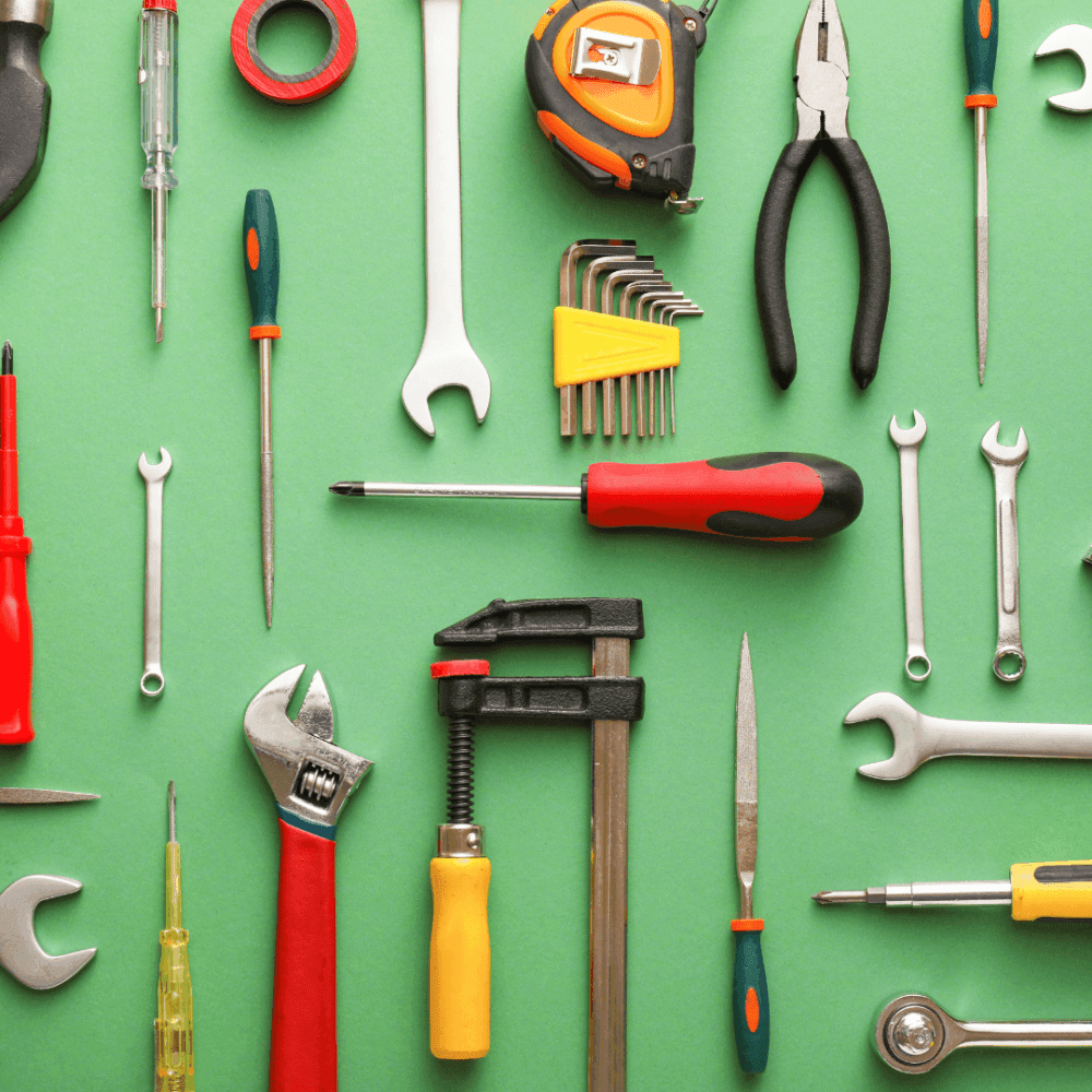 Assorted hand tools, including wrenches, screwdrivers, pliers, and Allen keys, neatly arranged on a green background. - Home Instead