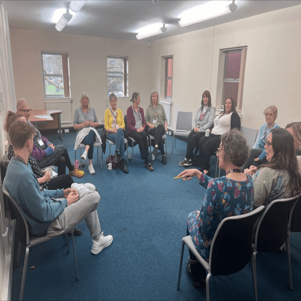 A group of people sitting in a circle in a brightly lit room, engaging in a discussion. - Home Instead