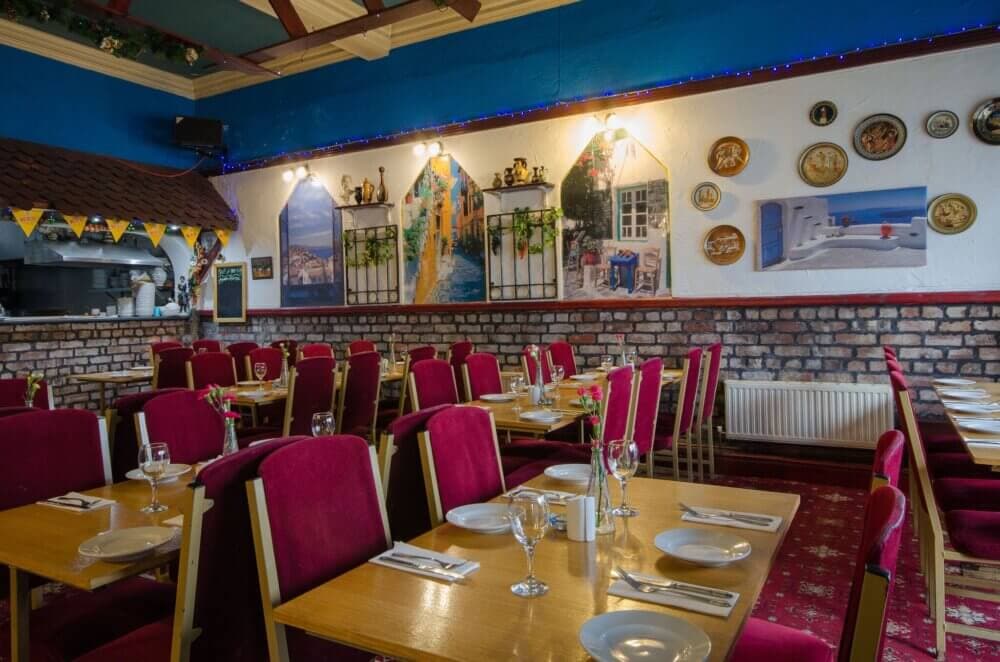 A colorful restaurant with red chairs and wooden tables set for dining, decorated with vibrant wall murals and plates. - Home Instead