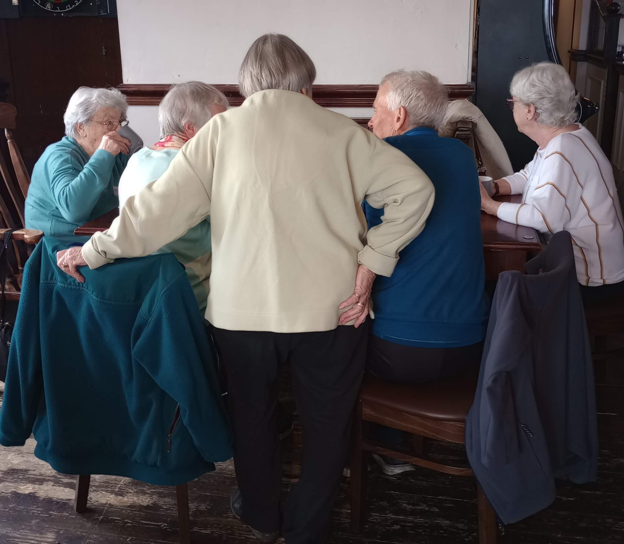 Group of elderly people sitting around a table, chatting and enjoying each other's company in a cozy indoor setting. - Home Instead